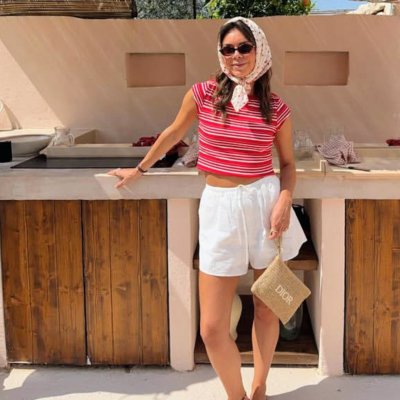 Pessoa com roupa casual vermelha e branca com bolsa Dior à frente de balcão de madeira em área exterior