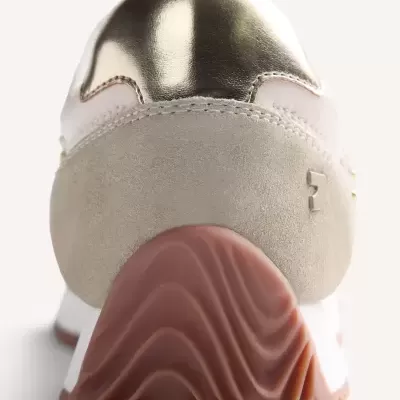 Parte traseira de sapatilha branca com salto nude ondulado e detalhe dourado