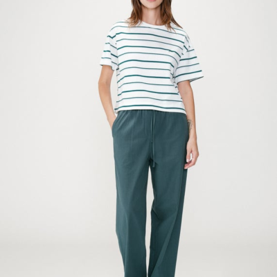 mulher com t-shirt branca riscada verde e calças largas verde-azul