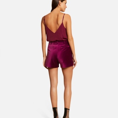 Mulher com top roxo e calções roxos, sandálias e meia-calça negras, vista de costas.