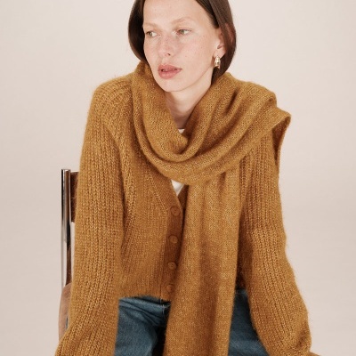 Mulher com cardigan e cachecol mostarda de malha grossa e calça jeans azul.