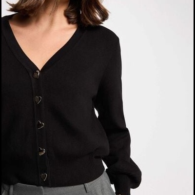 Mulher com cárdigan preto de botões em forma de coração e calças cinzentas.
