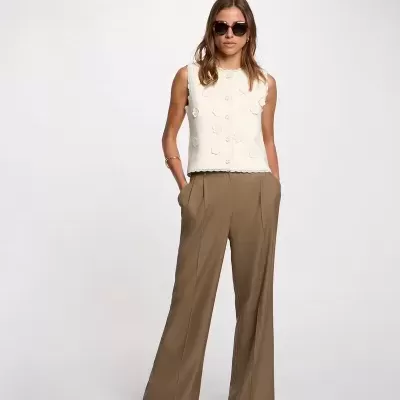 Mulher com colete branco e calças castanhas em fundo branco