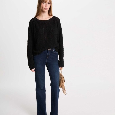 Mulher com camisola preta, calças de ganga azul escuro e mala castanha com franjas