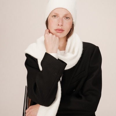 Mulher com gorro e cachecol brancos e casaco preto sentada