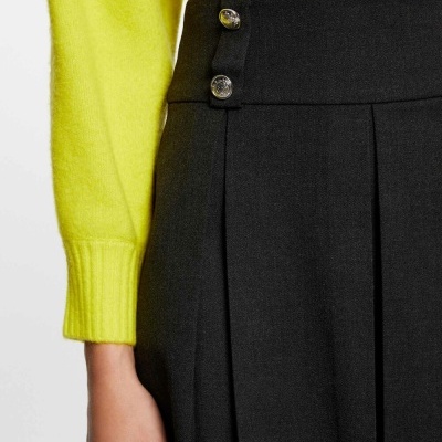 Vista parcial de saia preta plissada com botões prateados e camisola amarela