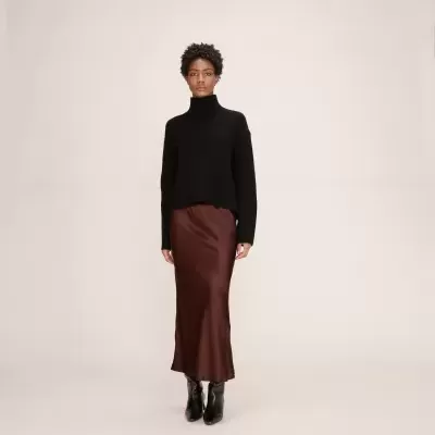 Mulher com vestido cetim castanho e pulôver preto em fundo claro