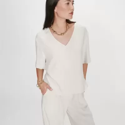 Conjunto de roupa bege para mulher em linho com acessórios dourados, em fundo branco