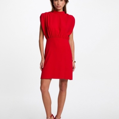 Modelo veste vestido vermelho curto com ombros almofadados e sandálias vermelhas.