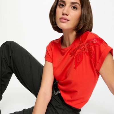 Mulher com t-shirt vermelha bordada e calças pretas sentada