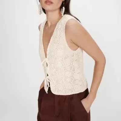 Blusa de crochet bege claro com padrões circulares e laços, usada com calças castanhas largas