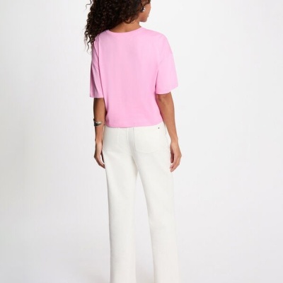 Mulher de costas com t-shirt rosa e calças brancas em fundo branco