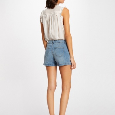 Mulher de costas a usar shorts de ganga azuis claros, blusa branca sem mangas com folhos e sandálias castanhas de tiras.