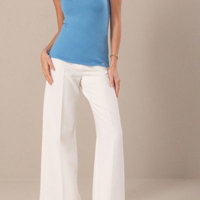 Mulher vestindo top azul e calças brancas com sapatos bege em fundo cinza