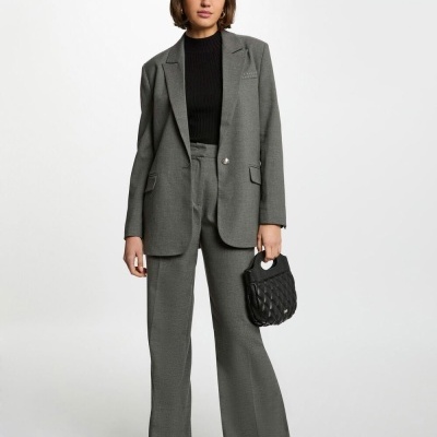 Mulher vestida com fato cinza formal e t-shirt preta, segurando bolsa preta acolchoada