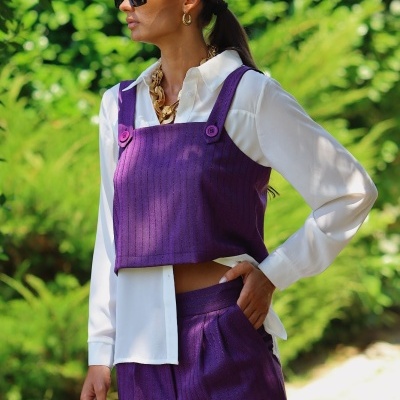 Mulher vestindo conjunto roxo com camisa branca e acessórios dourados ao ar livre