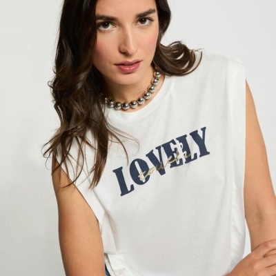 Mulher a usar t-shirt branca sem mangas com texto LOVELY em azul e colar prateado