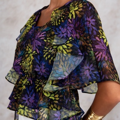 Blusa feminina transparente com padrão floral colorido e detalhes em babados.