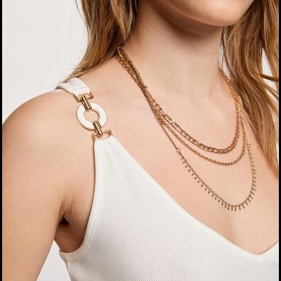 Mulher com top branco de alças com argolas douradas e colar dourado em várias camadas