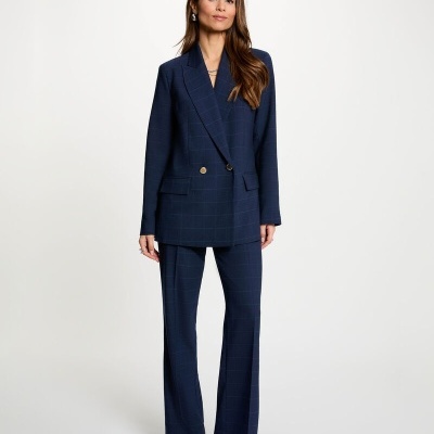 Mulher com blazer azul escuro e calças compridas combinando, com padrão de riscas finas, em fundo branco.