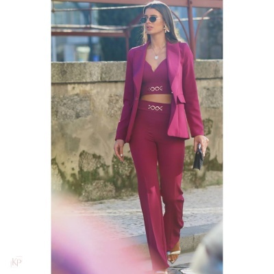 Conjunto feminino rosa com blazer, top e calças ao ar livre junto a parede de pedra