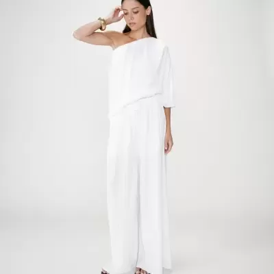 Mulher vestindo conjunto branco plissado com blusa de uma manga e calças largas.