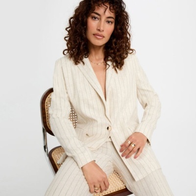 Conjunto feminino creme com riscas verticais, blazer e calças, sentado numa cadeira de madeira com palhinha.
