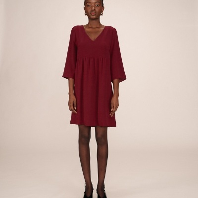 Homem numa sala a vestir vestido bordô com decote em V e mangas 3/4