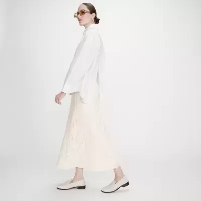 Mulher com camisa branca, saia rendada creme, sapatos baixos creme e óculos amarelos