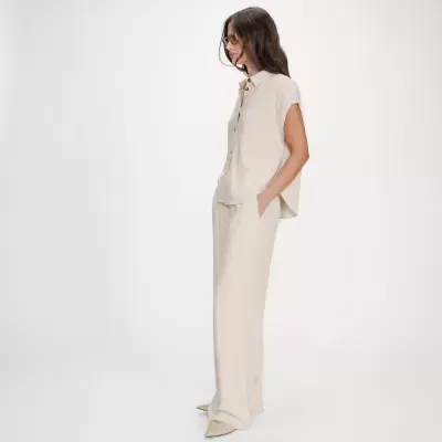 Conjunto feminino bege claro com camisa e calças largas, sapatos bege, fundo branco