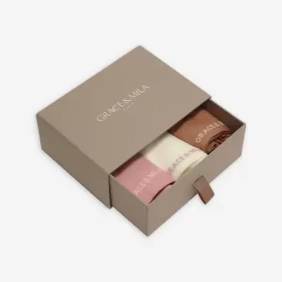 Caixa cinza com três meias rosa, branco e castanho dentro, texto GRACE + MILA HARLEM na tampa