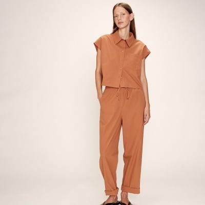 Conjunto feminino castanho claro com camisa sem mangas e calças, sandálias pretas, fundo neutro.