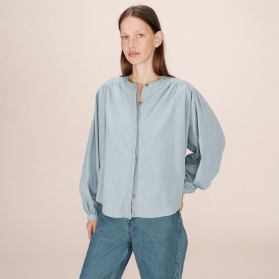 Mulher veste blusa azul clara de tecido com mangas bufantes e calças de ganga azul