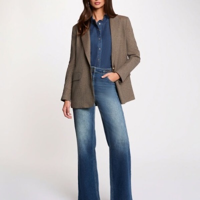 Mulher com blazer castanho, camisa denim e jeans azul em fundo branco