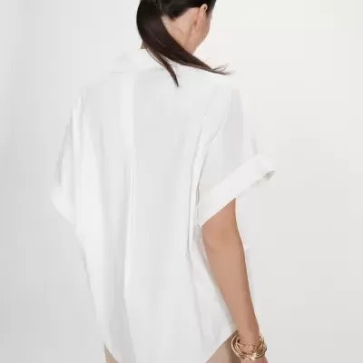 Blusa branca de manga curta vista de costas com mulher usando pulseiras douradas