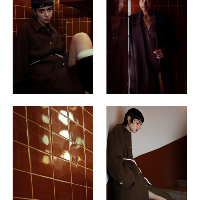 Casacos castanhos escuros com botões dourados e cordão branco, usados por duas modelos em interior com azulejos castanhos e paredes bicolores.