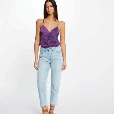 Mulher com top roxo e calças de ganga azul claro em fundo branco