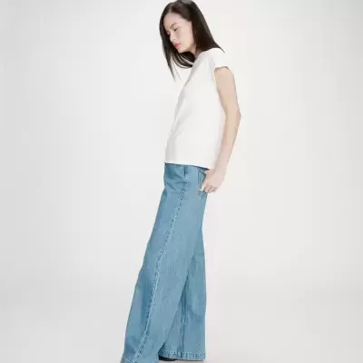 Mulher com t-shirt branca e calças de ganga largas azuis em fundo branco