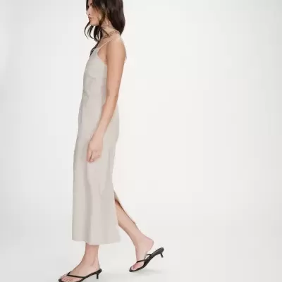 Vestido midi bege com alças finas e fenda, sandálias pretas de salto baixo.