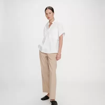 Mulher com camisa branca, calças bege e sapatos pretos em fundo branco