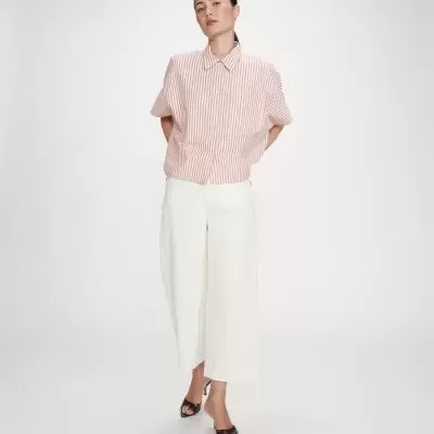 Mulher a usar top riscado rosa e branco com calças largas brancas e sapatos de salto preto