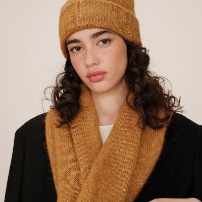 Mulher com gorro e cachecol castanho em fundo neutro