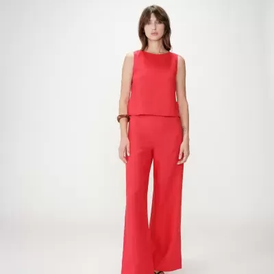 Mulher com conjunto vermelho de regata e calças largas com sandálias pretas e pulseira castanha em fundo branco.