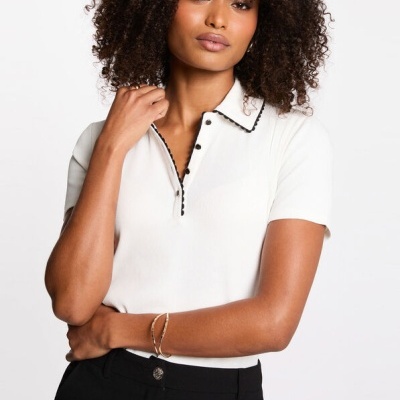 Modelo a usar camisola polo branca com detalhes pretos e calças pretas.