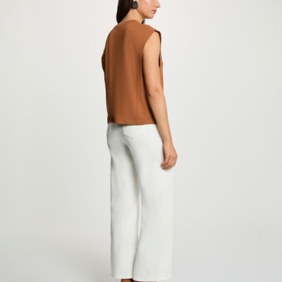 Mulher de costas com colete castanho, calças brancas largas e botas castanhas de salto.