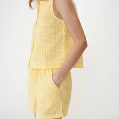 Conjunto feminino amarelo claro xadrez com camisa sem mangas e calções, bolsos e botões.