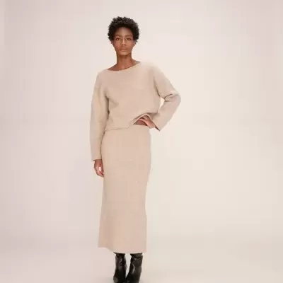 Conjunto feminino bege de malha com camisola de manga longa e saia comprida, botas pretas.