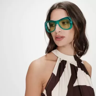 Mulher com óculos de sol verde e vestido com padrão castanho e creme