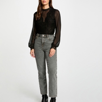 Blusa preta rendada com mangas compridas e calças de ganga cinza com botins pretos num fundo branco