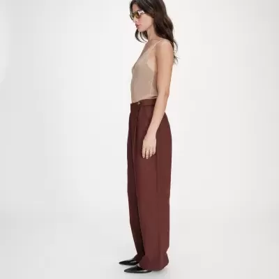 Mulher de perfil com top bege e calças largas castanho bordô em fundo branco